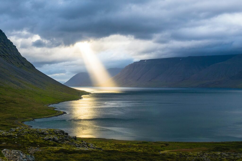 solrefleksjon på rolig vann nær grønne fjell